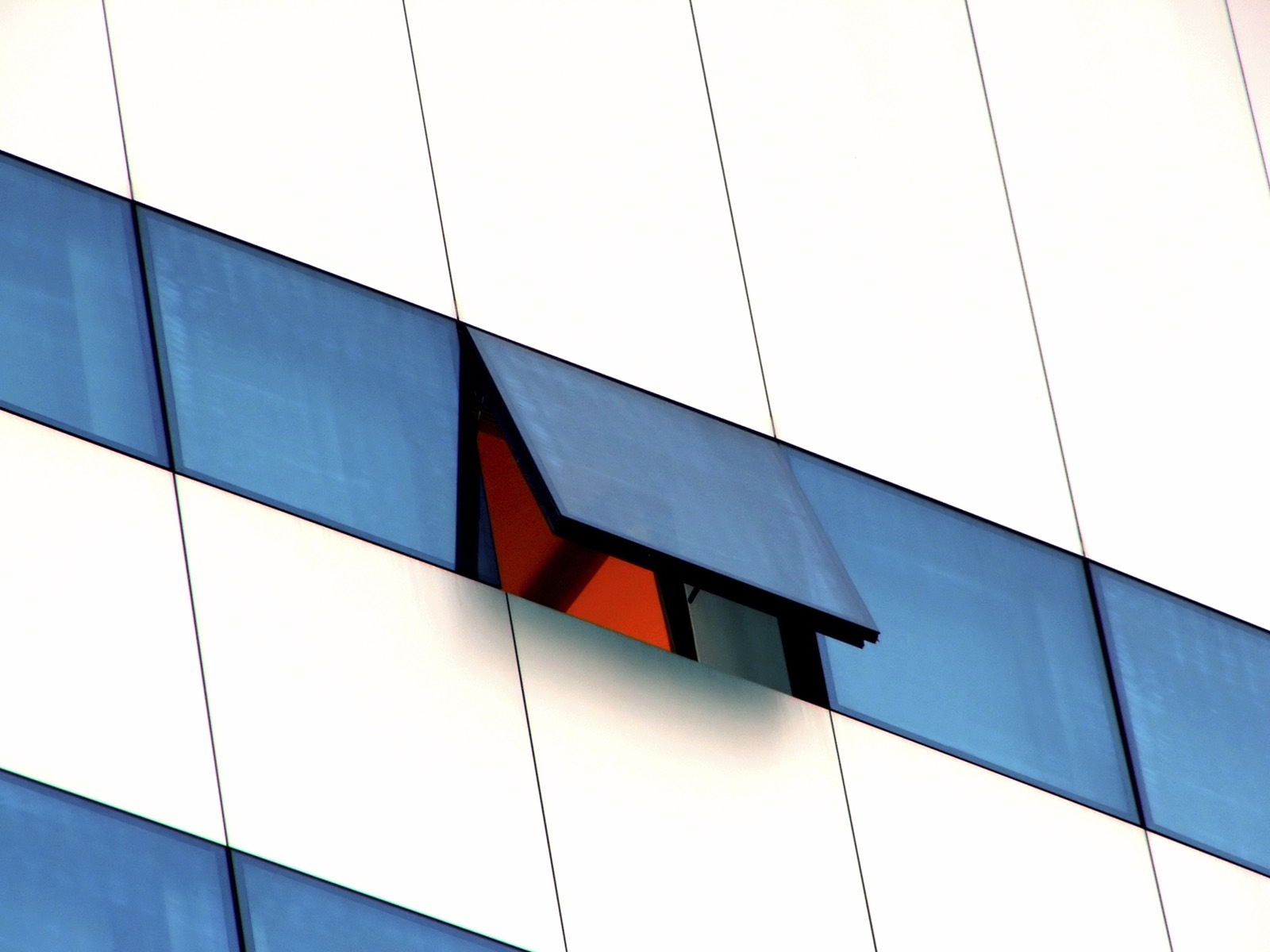 A blue glass facade with one window opened onto orange